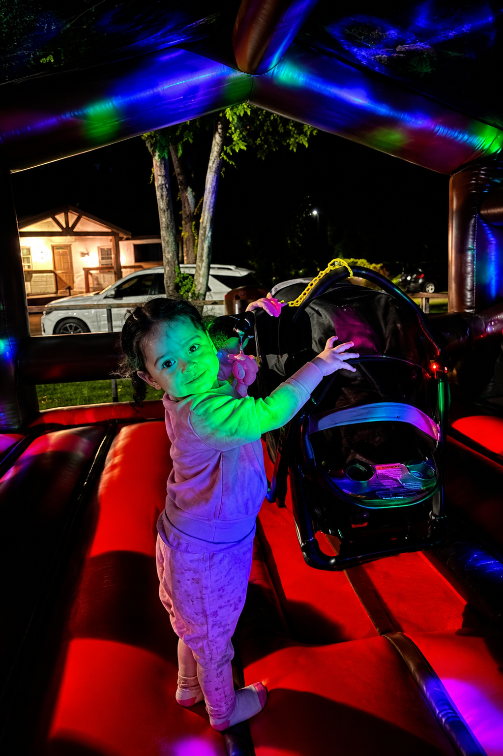 Toddler smiling inside a bounce house lit up with colorful disco lights at night