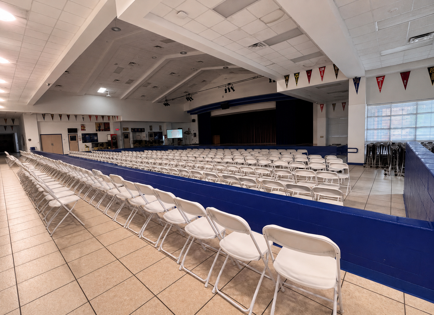 Rows of white folding chairs neatly set up facing a stage in an event hall